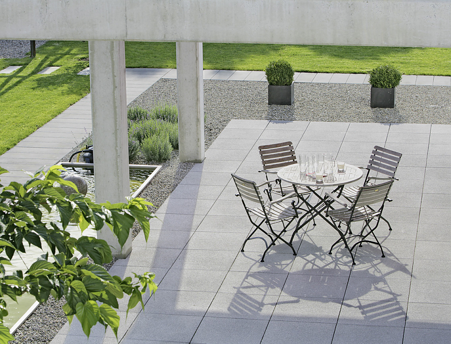 ARCADO Terrassenplatten aus Beton in der Farbe Opalgrau verlegt auf einer Terrasse mit Stühlen und einem Tisch