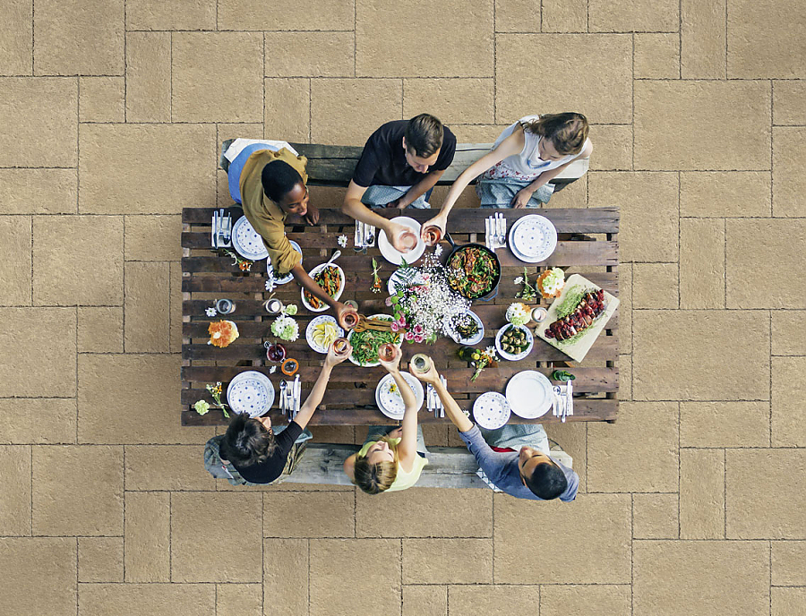 Mehrere Menschen sitzen an einem Tisch auf einer Terrasse mit SANTURO Terrassenplatten im Römischen Verband