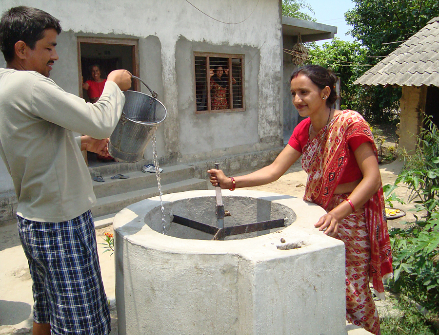 Eine nepalesische Frau und ein Mann befüllen eine Kleinbiogasanlage.