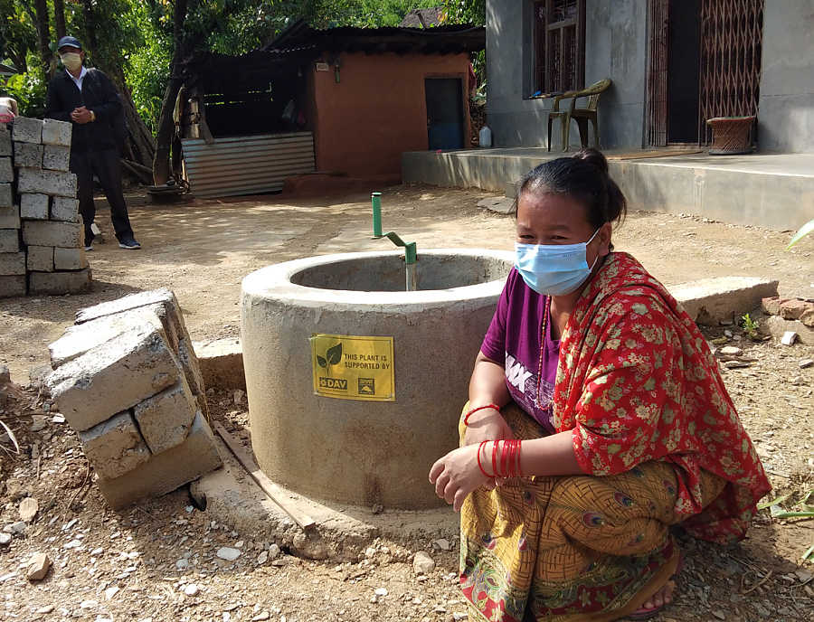 Eine nepalesische Frau sitzt neben einer Kleinbiogasanlage.