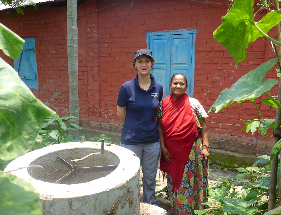 Eine nepalesische Frau steht mit einer anderen Frau neben einer Kleinbiogasanlage.