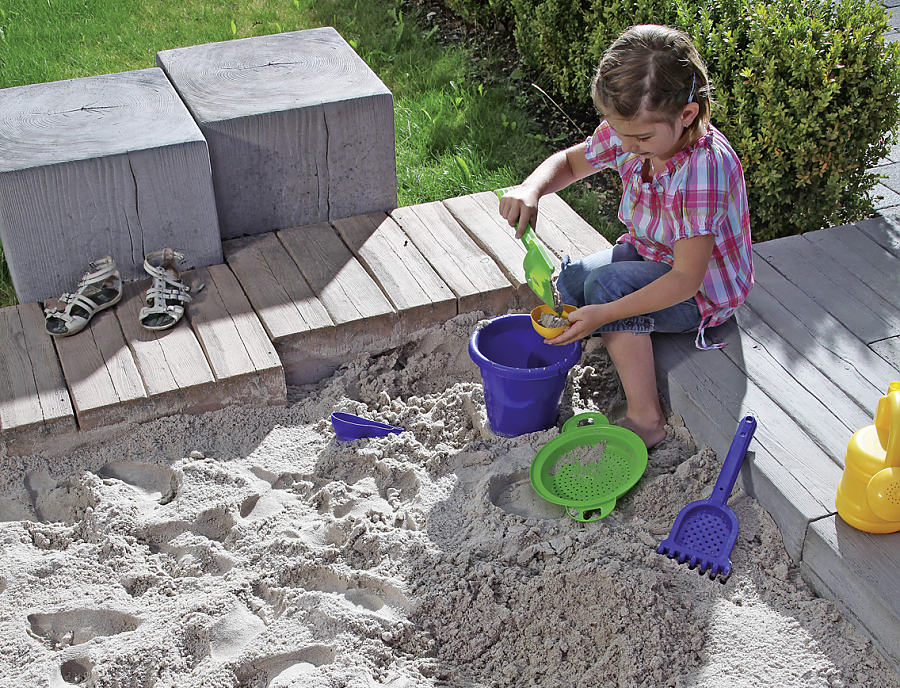 MAHORA TRIO Holzstrukturstein, Farbe Meranti und MAHORA Balken, Holzstrukturstein kombiniert zu einem Sandkasten in dem ein Kind spielt