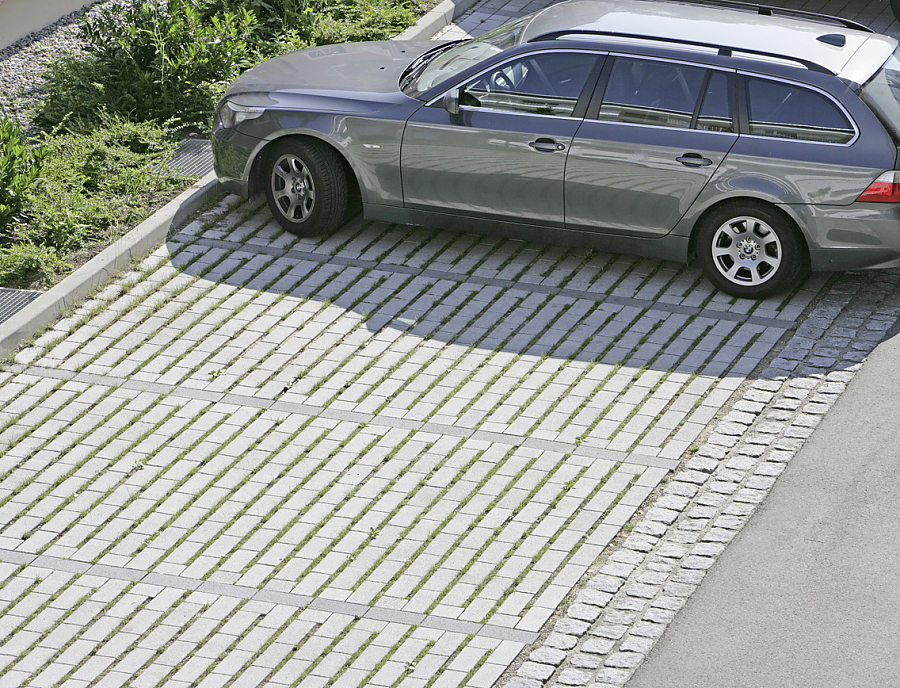 Wasserdurchlässiger Pflasterstein ARCADO Längsrasenfugenstein aus Beton in der Farbe Opalgrau verlegt als Parkfläche mit einem darauf parkenden Auto