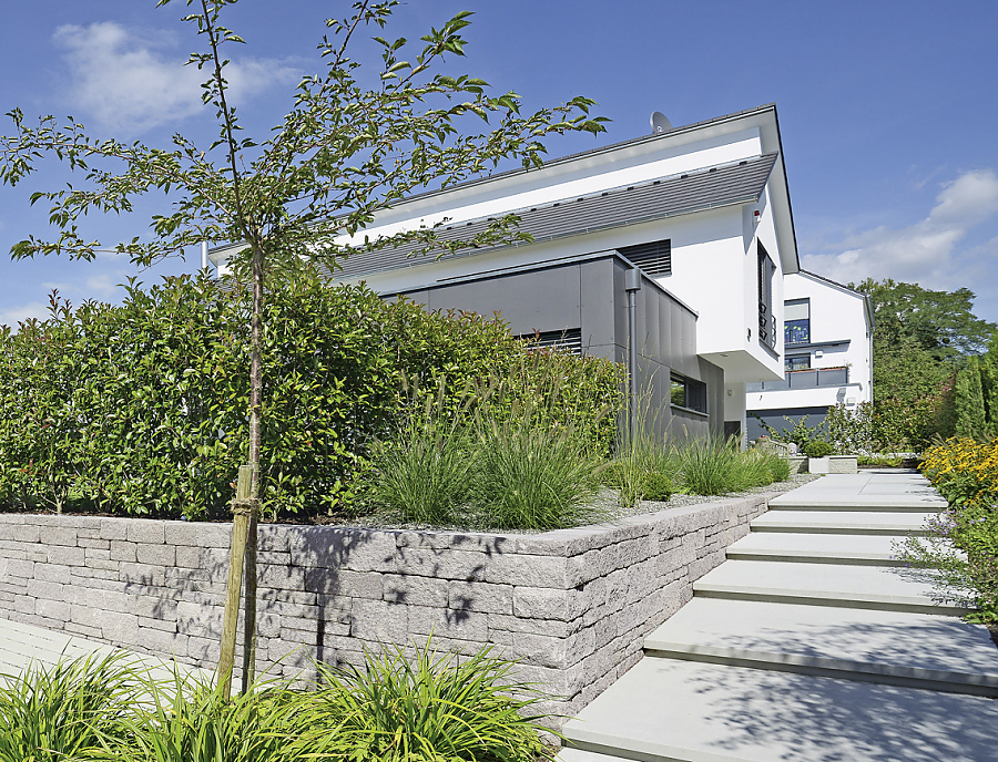 Gartenmauer SANTURO Landhausmauer in der Farbe Naturgrau passend zu dem grau-weißen Haus im Hintergrund 