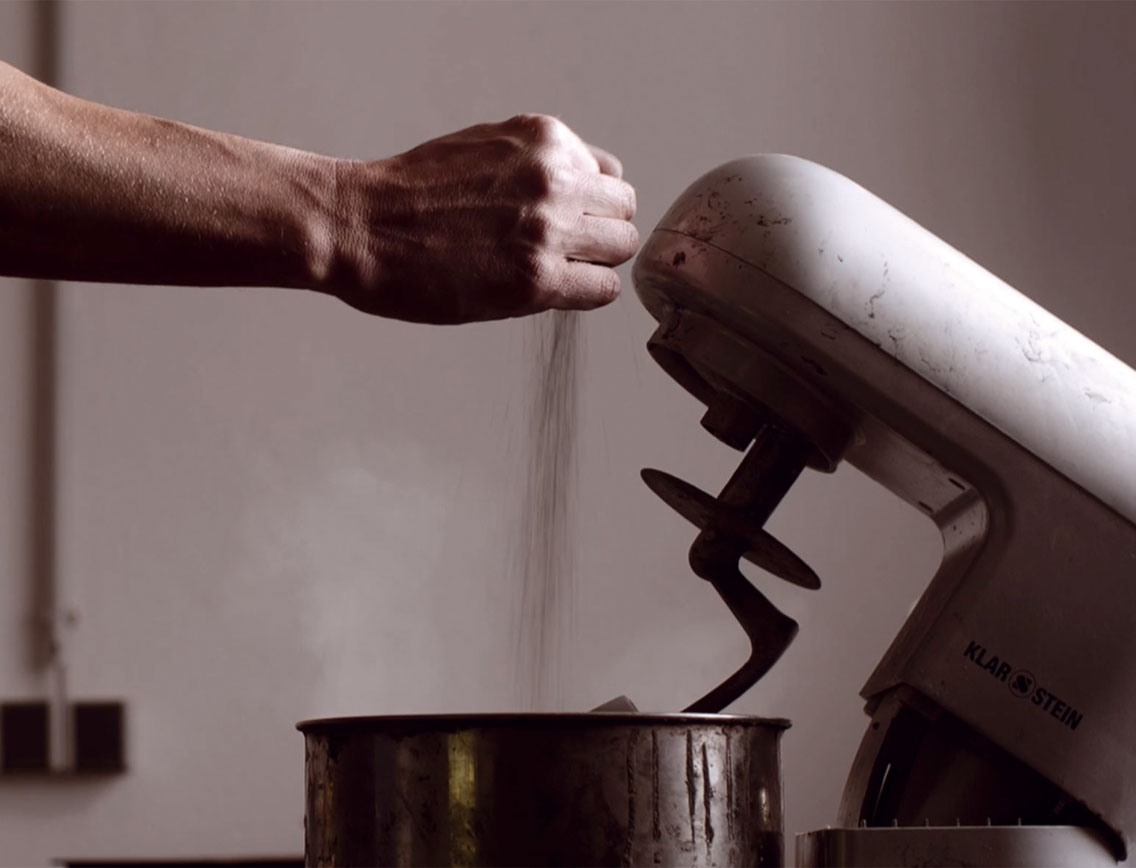 Eine Hand lässt Sand in einen Mixer rieseln.