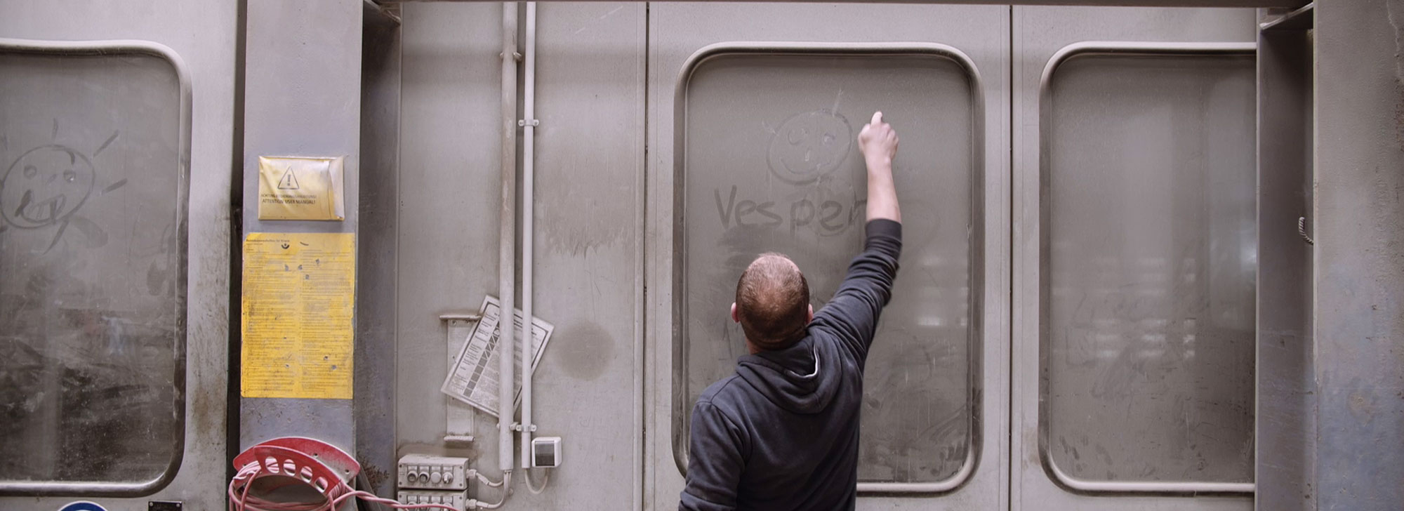 Ein Arbeiter schreibt in eine verstaubte Glastür "VESPER"
